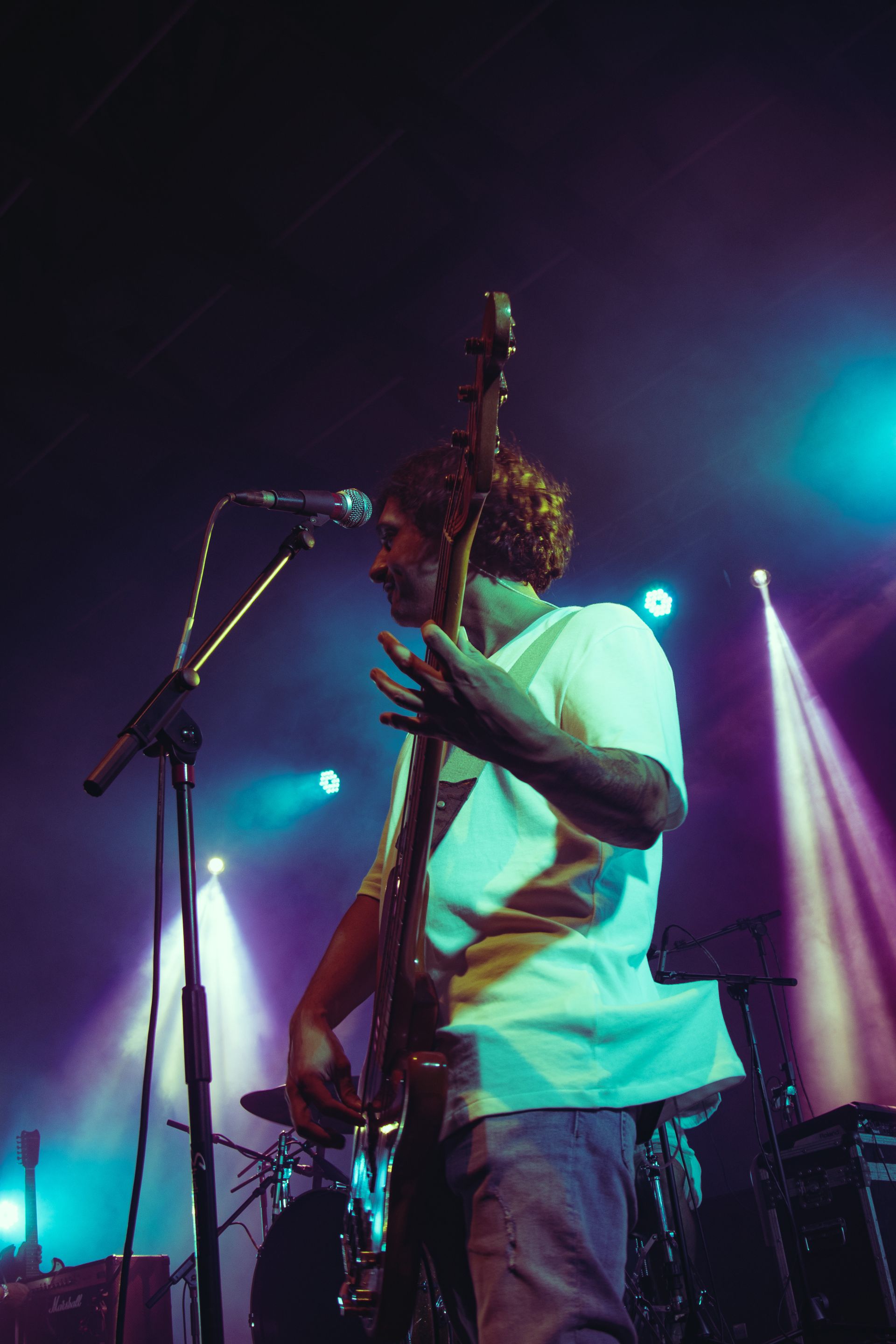 A bassist at the mic, beams crossing behind, from a low angle